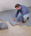 Contractors installing basement subfloor tiles and matting on a concrete basement floor in Irving, Texas